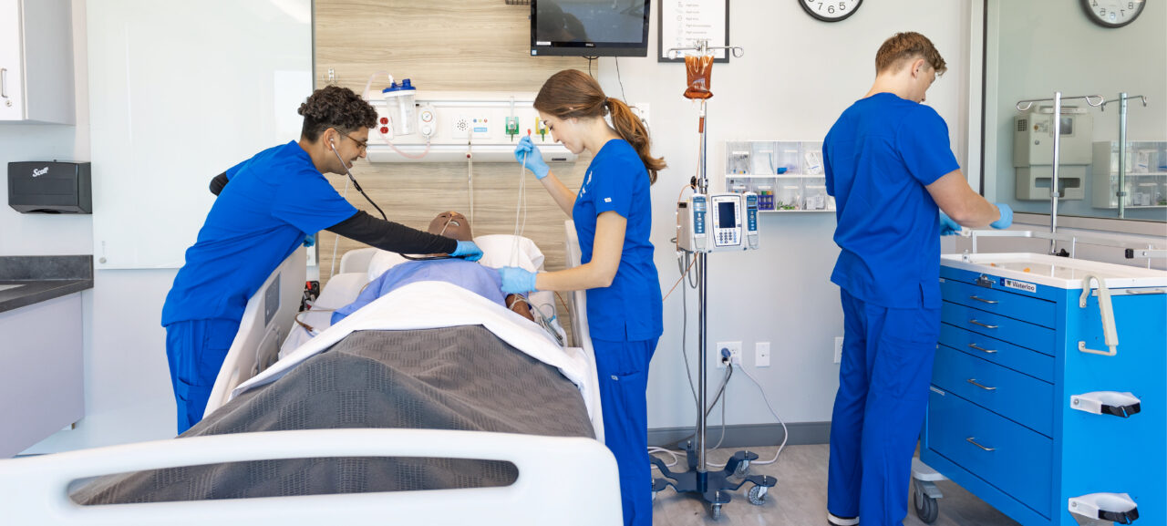 Joyce University nursing students in blue scrubs practicing in simulation lab on high fidelity mannequin