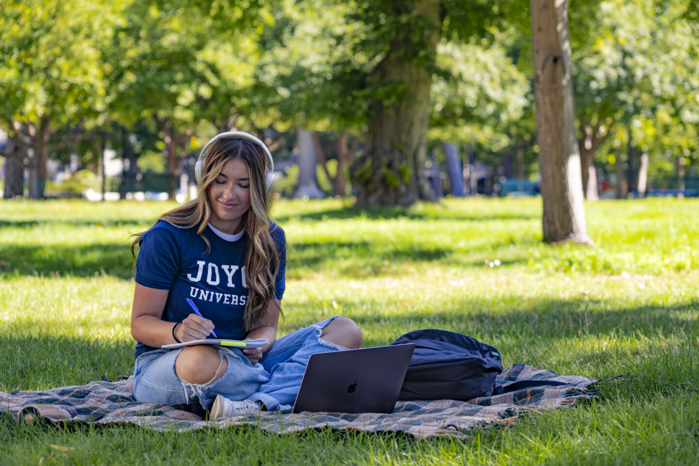 female joyce university nursing student sitting on a blanket in the park doing homework