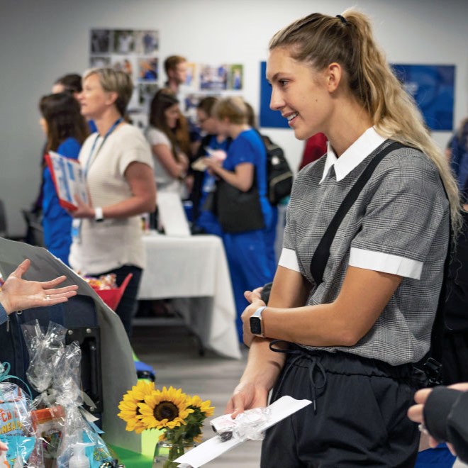 Female joyce university nursing student in business casual attire speaking to vendor at campus career fair