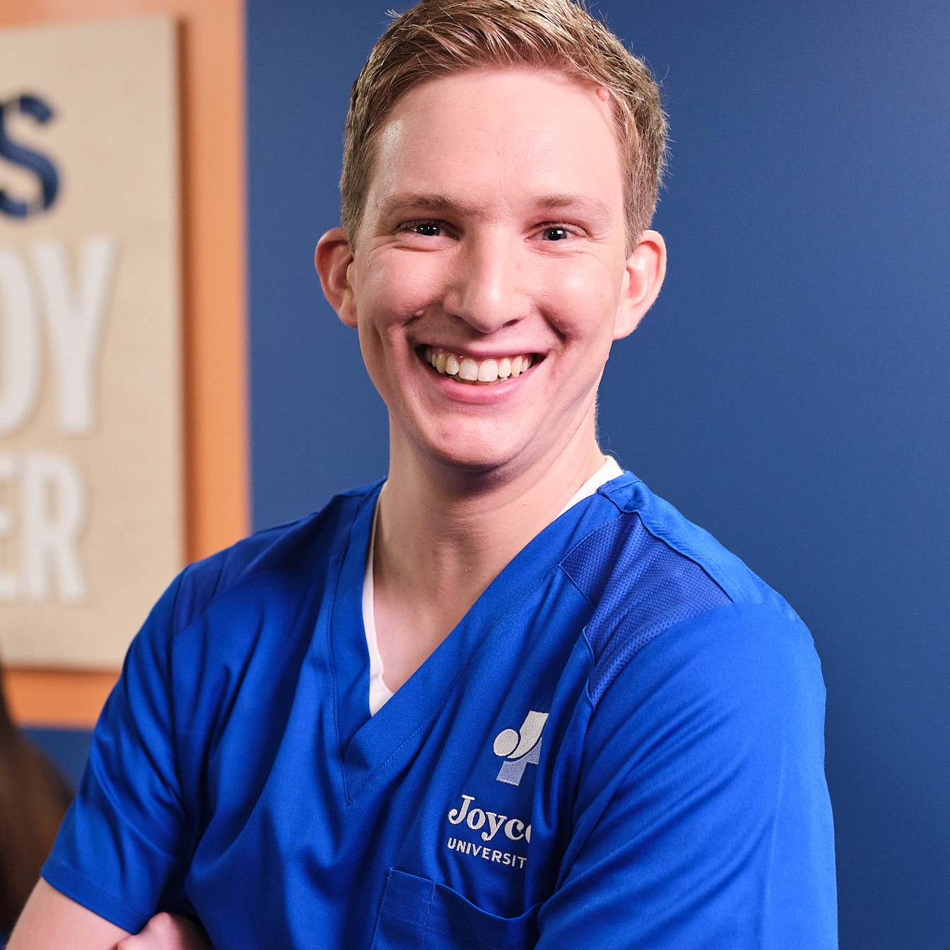 Blond male nursing student in blue scrubs standing in flo's study center on joyce university campus