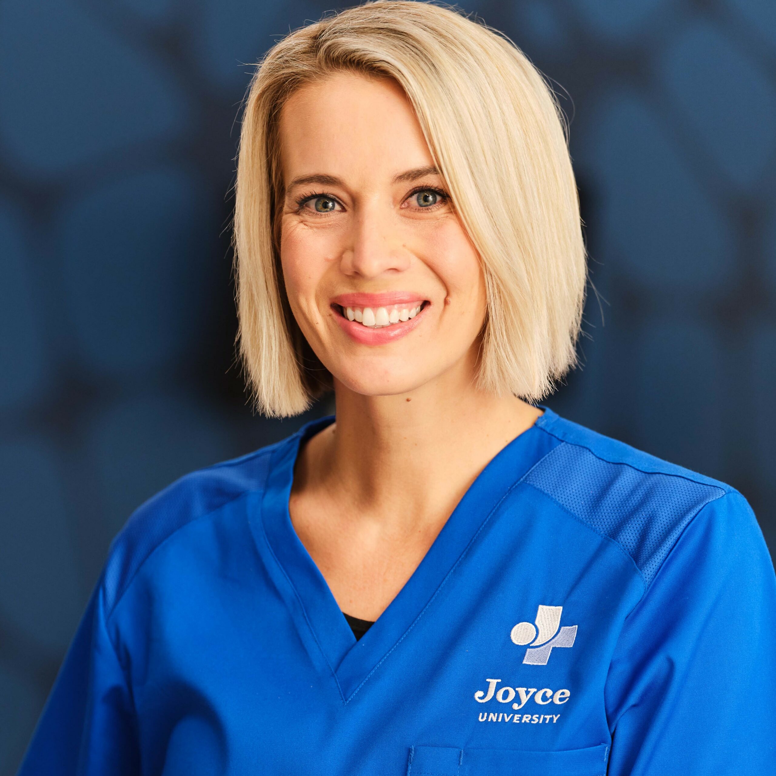 blonde female nursing student in blue joyce university scrubs standing in A & P lab