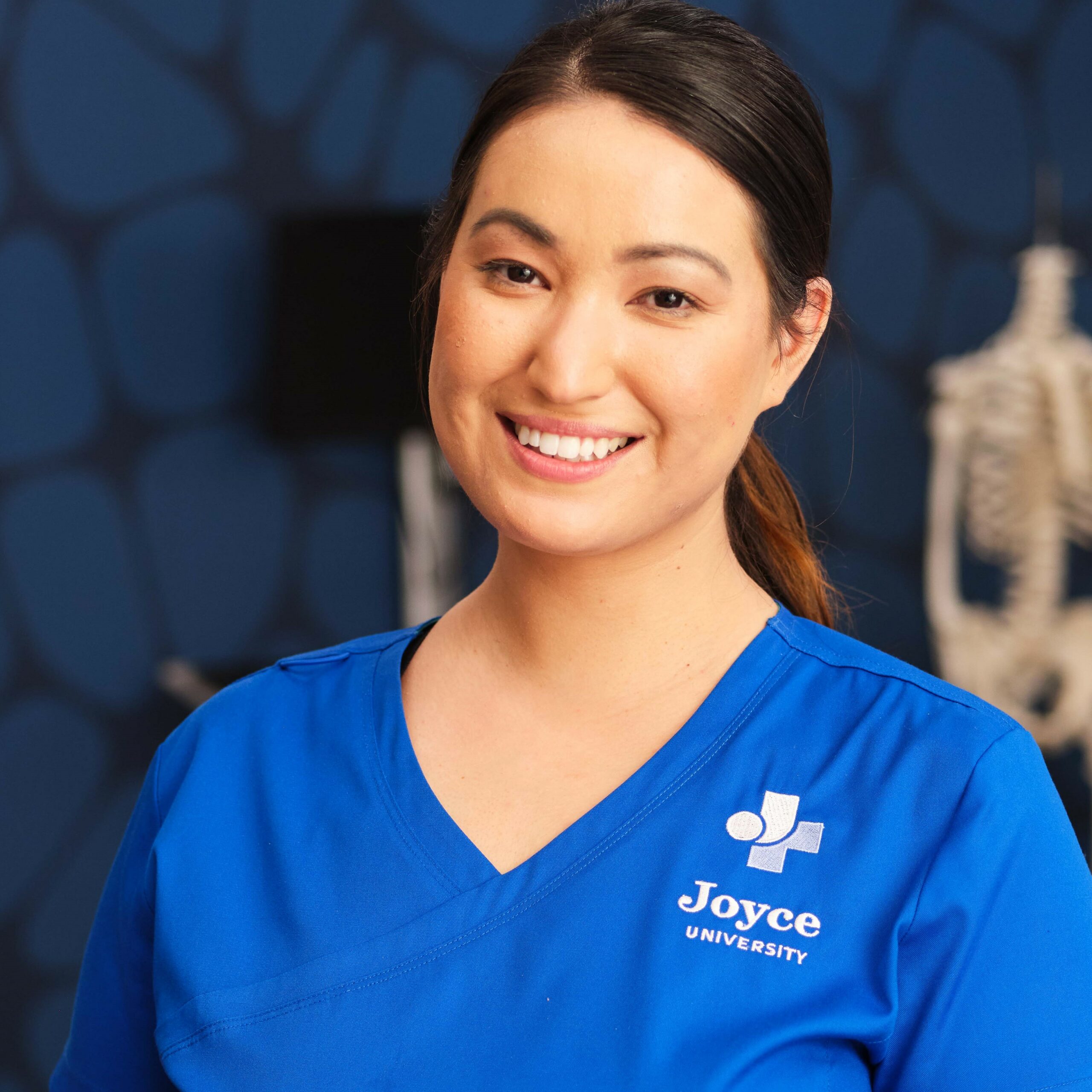 female nursing student smiling in blue joyce scrubs in A & P lab