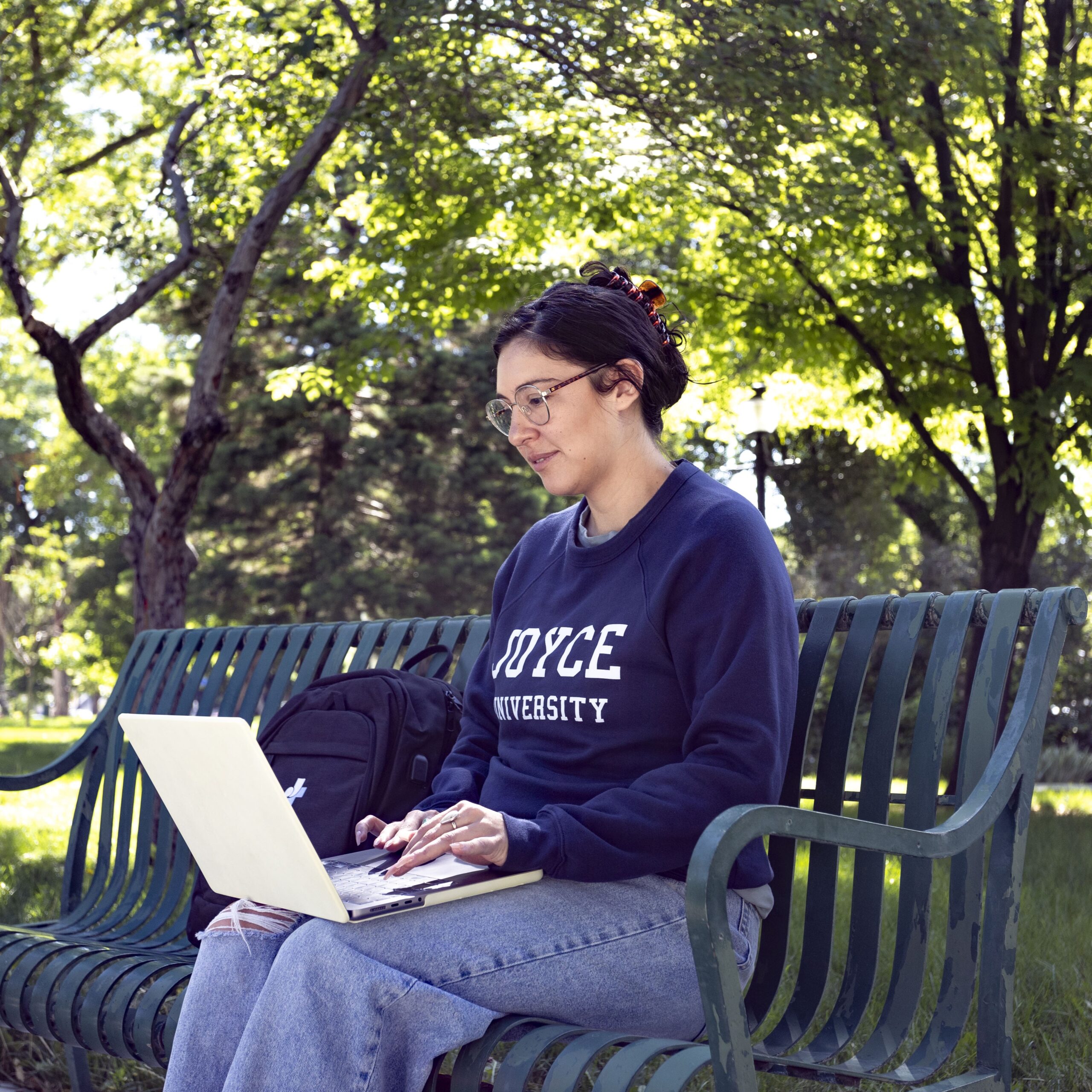 Joyce University nursing student sitting on park bench in Ohio studying on a laptop